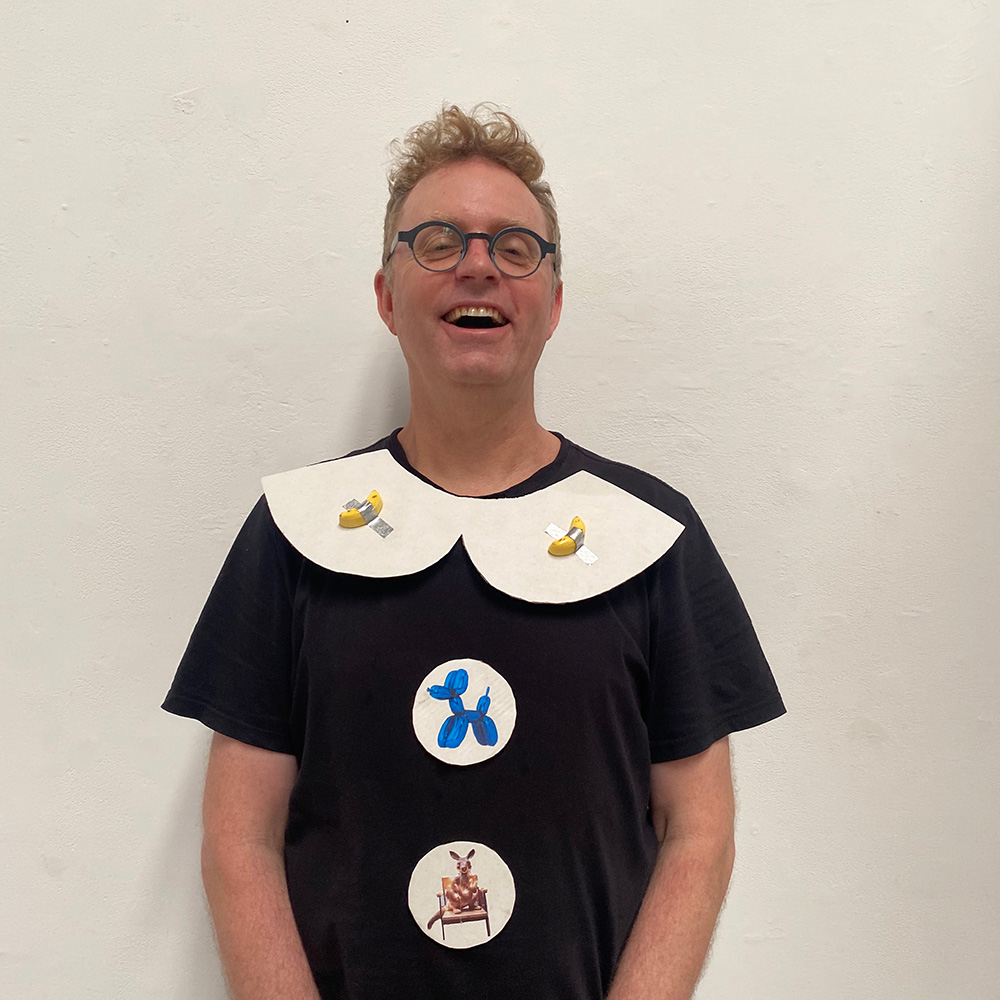 image of a person with light brown hair and glasses laughing and wearing three artworks on his shirt